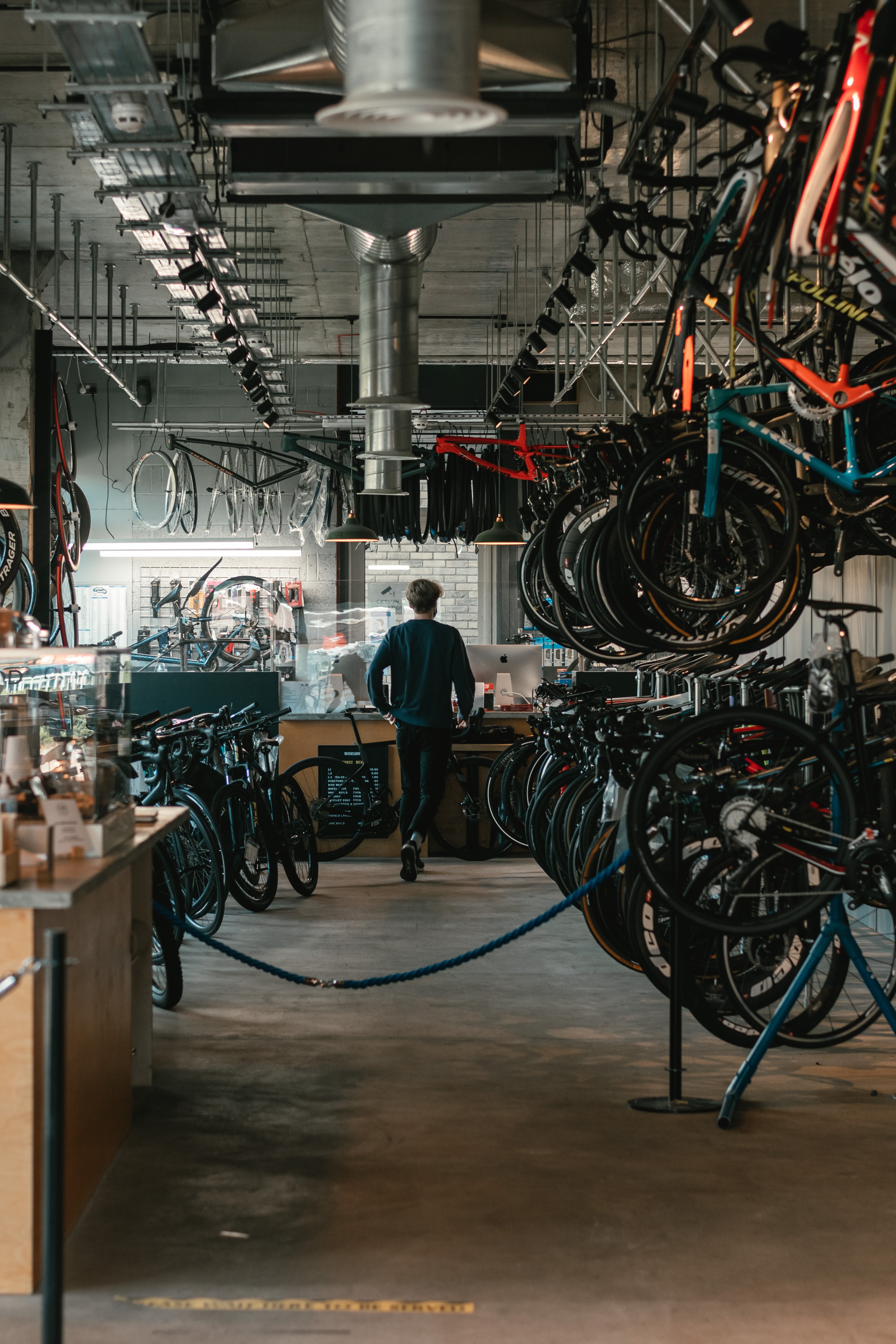 man walking toward a counter in a bike shop surrounded bikes on the ground and hanging